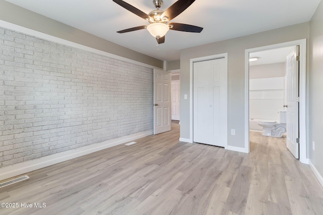 unfurnished bedroom with ensuite bathroom, a closet, ceiling fan, brick wall, and light hardwood / wood-style floors