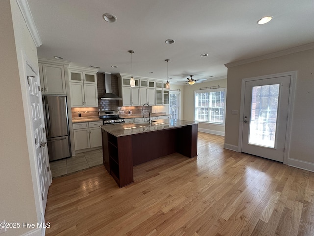 kitchen with a sink, appliances with stainless steel finishes, crown molding, wall chimney range hood, and tasteful backsplash