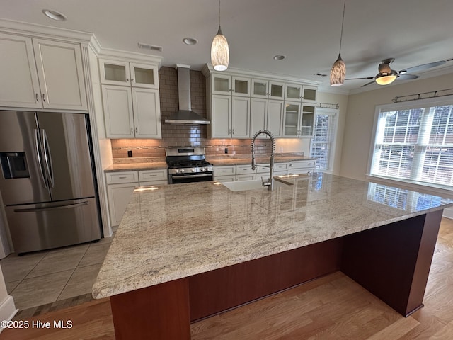 kitchen with visible vents, a sink, backsplash, appliances with stainless steel finishes, and wall chimney range hood