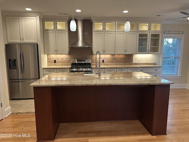 kitchen featuring visible vents, a sink, backsplash, stainless steel appliances, and wall chimney exhaust hood