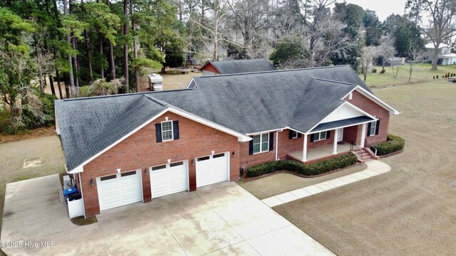 view of front of property with driveway, roof with shingles, covered porch, an attached garage, and brick siding