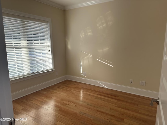 spare room with crown molding, wood finished floors, and baseboards