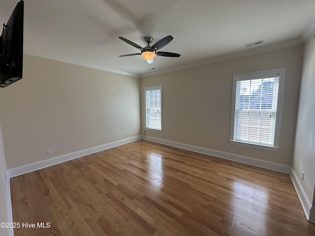 empty room featuring crown molding, wood finished floors, baseboards, and a wealth of natural light