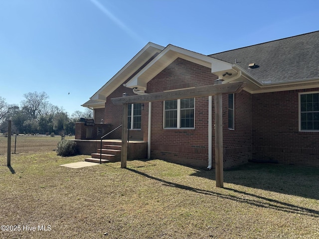 view of property exterior with brick siding, a lawn, fence, and roof with shingles