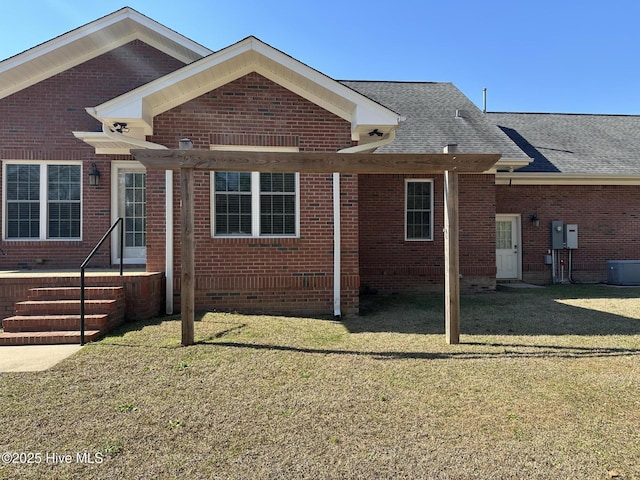 view of front facade featuring a front yard, brick siding, central AC, and roof with shingles