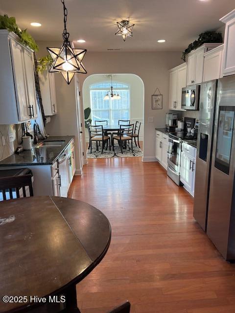 kitchen with sink, white cabinets, hanging light fixtures, stainless steel appliances, and light wood-type flooring