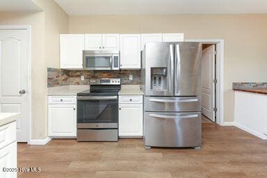 kitchen with stainless steel appliances, white cabinetry, light hardwood / wood-style floors, and decorative backsplash