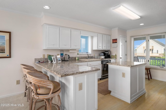 kitchen featuring white cabinetry, black dishwasher, sink, kitchen peninsula, and light stone countertops