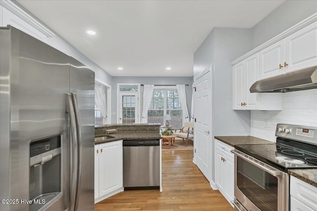 kitchen featuring appliances with stainless steel finishes, white cabinetry, dark stone countertops, decorative backsplash, and light hardwood / wood-style flooring