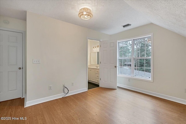 unfurnished bedroom with lofted ceiling, ensuite bath, wood-type flooring, and a textured ceiling