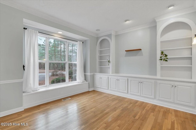 unfurnished room featuring crown molding, light wood-type flooring, and built in shelves