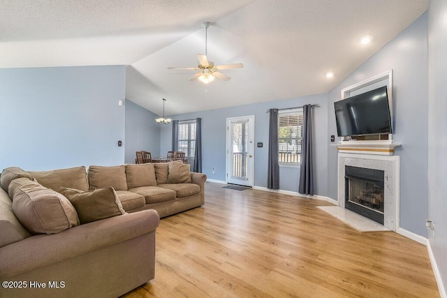 living room featuring light hardwood / wood-style flooring, ceiling fan with notable chandelier, a fireplace, and vaulted ceiling