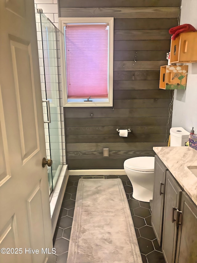 bathroom with toilet, an enclosed shower, vanity, wooden walls, and tile patterned flooring