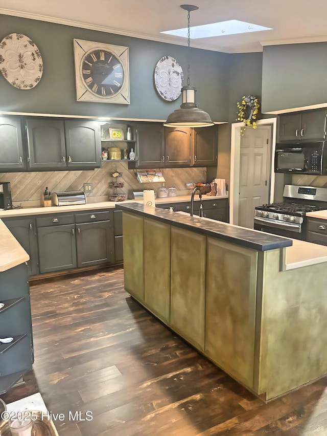 kitchen featuring dark wood-type flooring, ornamental molding, stainless steel range with gas cooktop, and a center island with sink