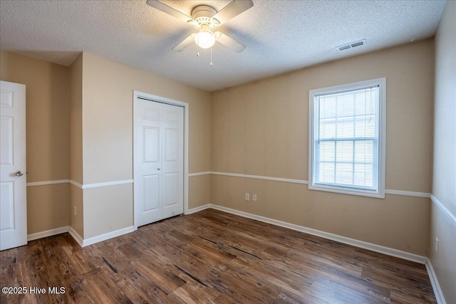 unfurnished bedroom featuring ceiling fan, dark wood-type flooring, a textured ceiling, and a closet