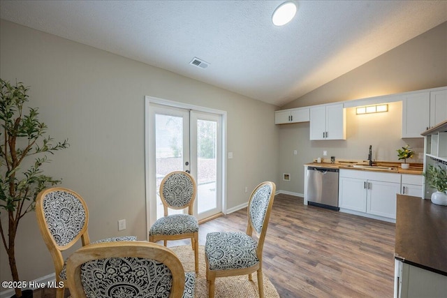 kitchen with sink, wooden counters, white cabinetry, vaulted ceiling, and stainless steel dishwasher