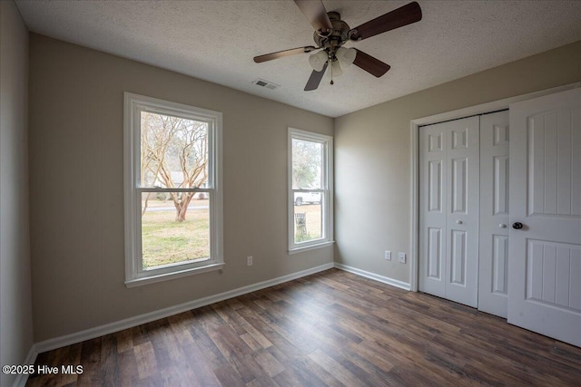 unfurnished bedroom with dark wood-type flooring, a closet, multiple windows, and a textured ceiling