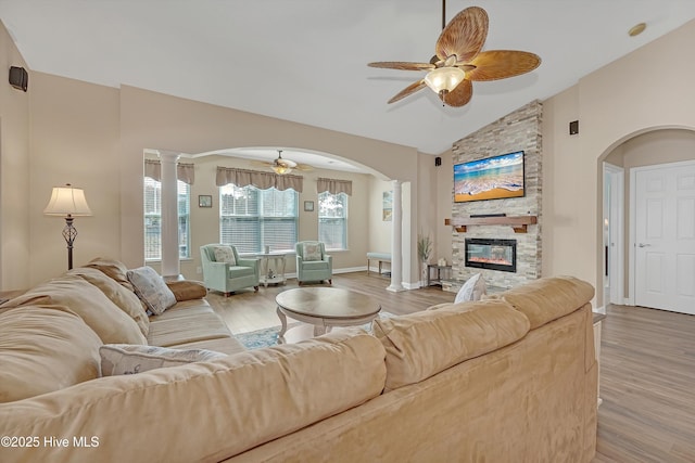 living room featuring ceiling fan, a fireplace, decorative columns, and light wood-type flooring