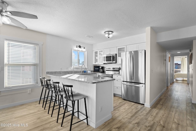 kitchen with a breakfast bar area, a peninsula, a sink, appliances with stainless steel finishes, and glass insert cabinets