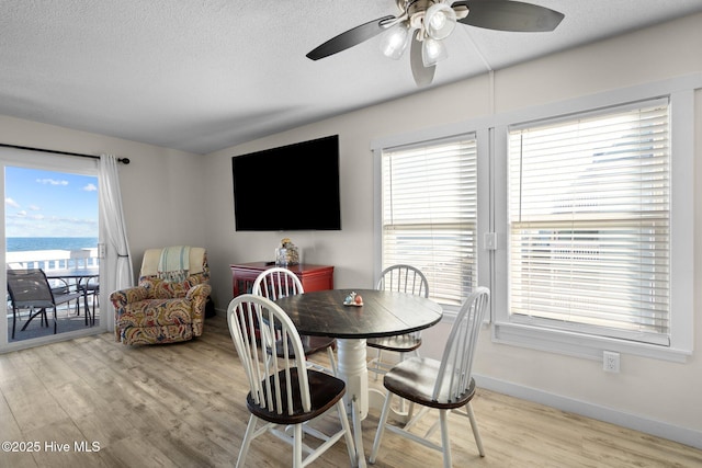 dining area with a ceiling fan, baseboards, light wood-style flooring, and a textured ceiling