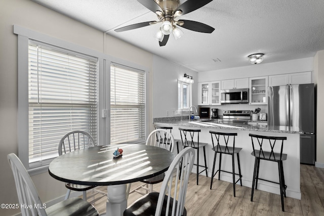 dining space with light wood-style floors, a ceiling fan, and a textured ceiling