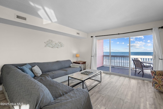 living room featuring a water view, light wood-type flooring, visible vents, and a textured ceiling