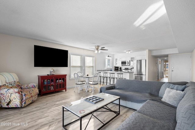 living area with light wood-style floors, ceiling fan, a textured ceiling, and baseboards