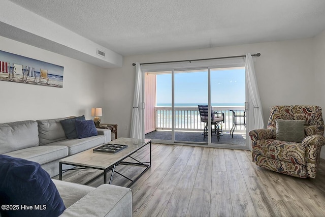 living room featuring a water view, light hardwood / wood-style flooring, and a textured ceiling