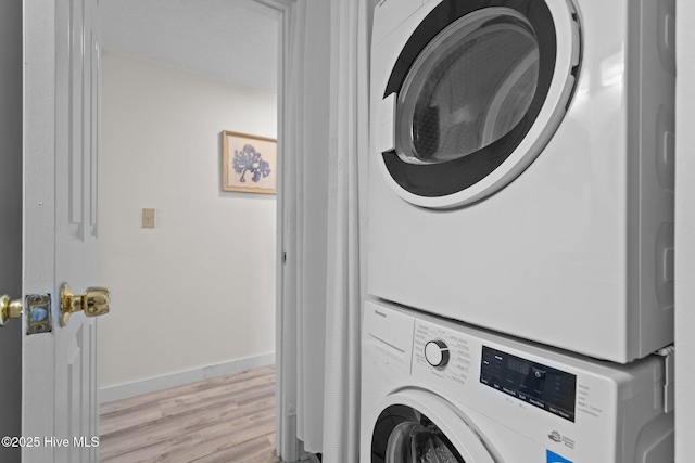 laundry room featuring light wood-type flooring, stacked washer / drying machine, laundry area, and baseboards