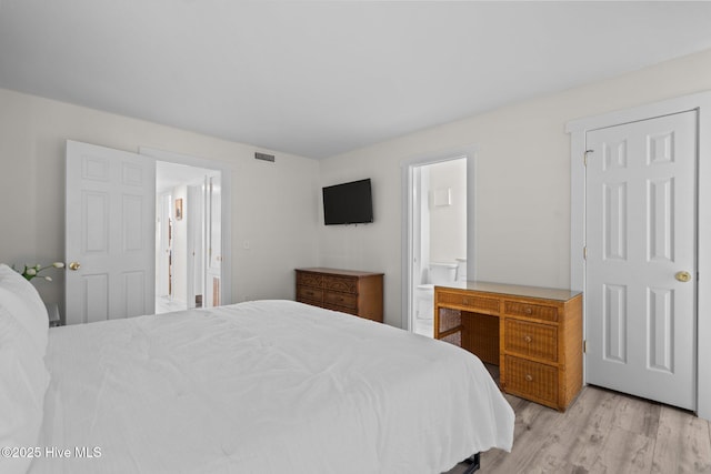 bedroom with light wood-type flooring, visible vents, and ensuite bath