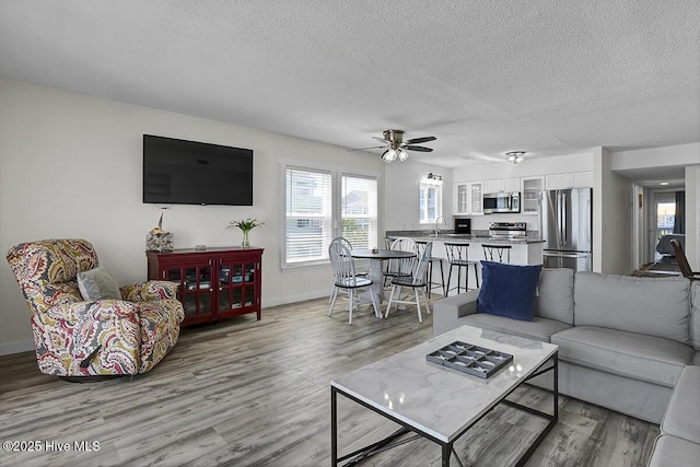 living room featuring sink, hardwood / wood-style flooring, a textured ceiling, and ceiling fan