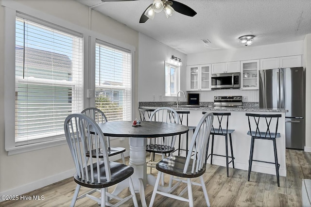 dining space with ceiling fan, sink, a textured ceiling, and light wood-type flooring