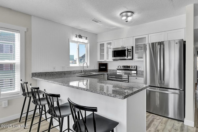 kitchen with white cabinetry, stainless steel appliances, kitchen peninsula, and sink