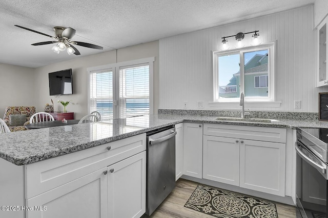 kitchen featuring sink, appliances with stainless steel finishes, light stone counters, white cabinets, and kitchen peninsula