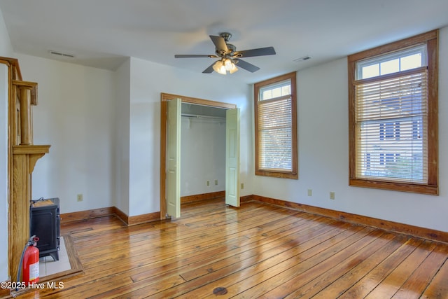 unfurnished bedroom featuring light hardwood / wood-style floors, a closet, ceiling fan, and a wood stove