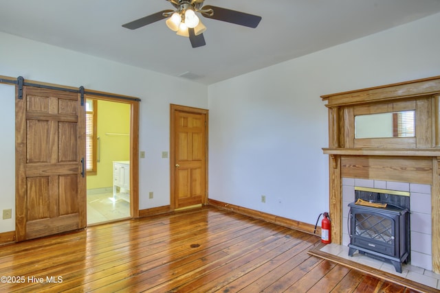 unfurnished living room featuring wood-type flooring, a barn door, a wood stove, and ceiling fan