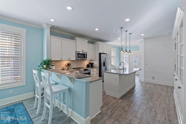 kitchen featuring decorative light fixtures, an island with sink, stainless steel appliances, light stone countertops, and white cabinets