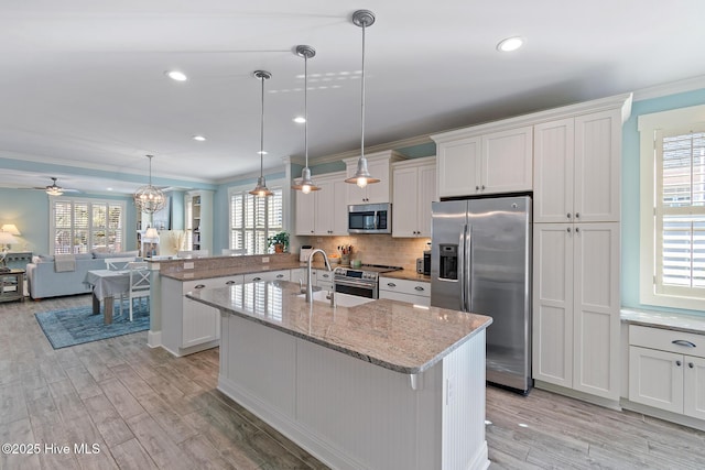 kitchen with white cabinetry, light stone counters, decorative light fixtures, appliances with stainless steel finishes, and an island with sink