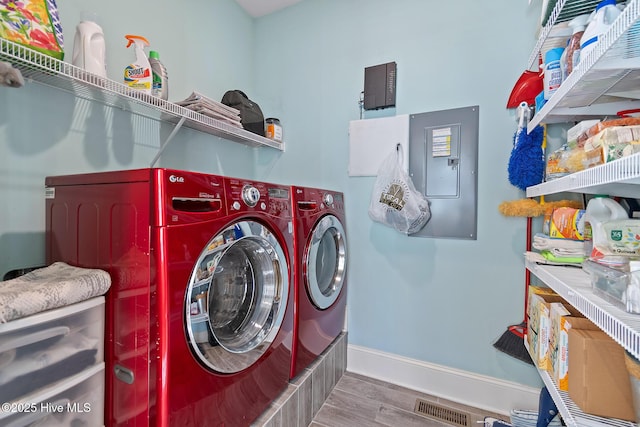 clothes washing area featuring hardwood / wood-style flooring, washer and clothes dryer, and electric panel