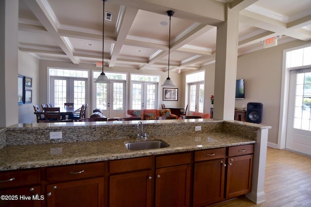 kitchen featuring french doors, sink, light stone counters, decorative light fixtures, and beamed ceiling