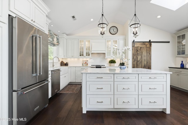 kitchen with stainless steel appliances, a barn door, vaulted ceiling, a kitchen island, and decorative backsplash