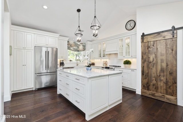 kitchen featuring high end refrigerator, lofted ceiling, white cabinets, a kitchen island, and glass insert cabinets
