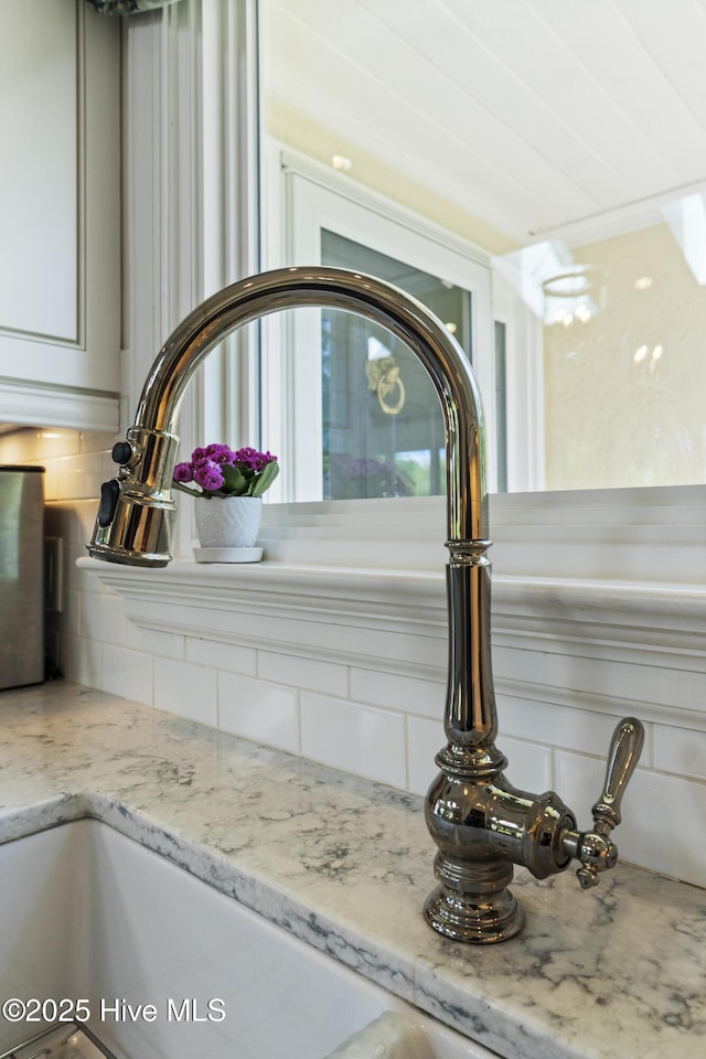 kitchen view of decorative backsplash, a sink, and light stone countertops
