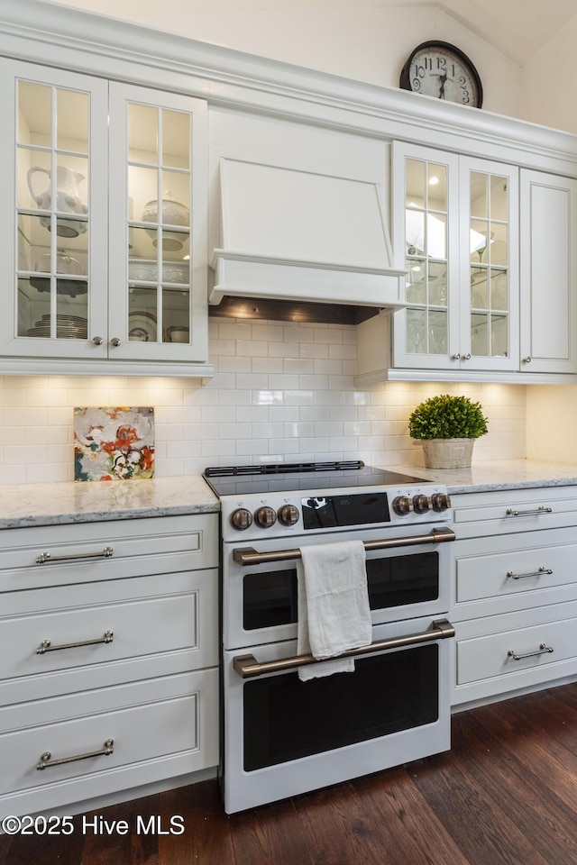 kitchen featuring double oven range, custom exhaust hood, white cabinetry, decorative backsplash, and light stone counters