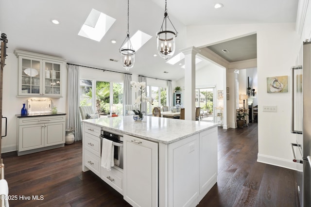 kitchen featuring vaulted ceiling, a skylight, oven, white cabinets, and glass insert cabinets