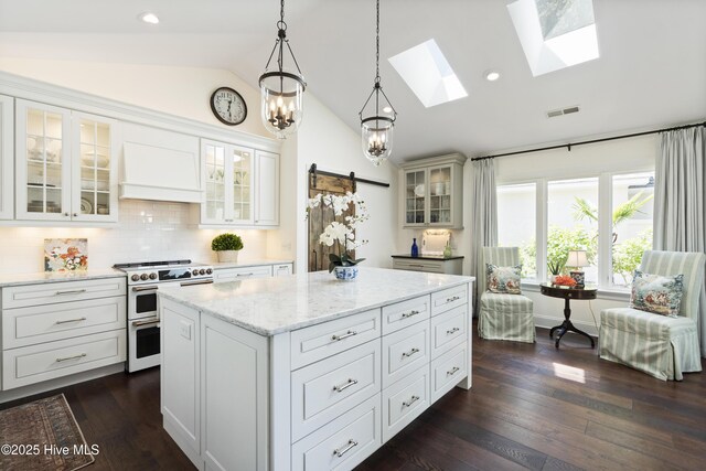 kitchen with double oven range, lofted ceiling, custom exhaust hood, a skylight, and light stone counters