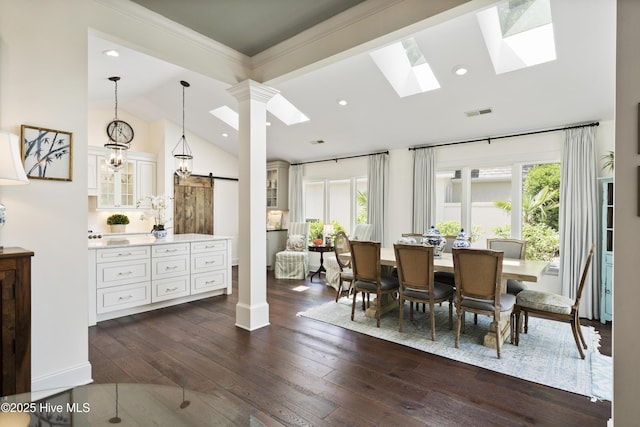 dining room with a barn door, plenty of natural light, dark wood-style floors, ornate columns, and ornamental molding