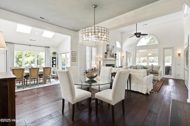 dining room with a fireplace, dark wood-style floors, a ceiling fan, a chandelier, and high vaulted ceiling