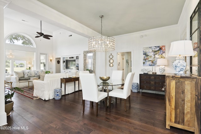 dining room featuring dark wood-type flooring, a ceiling fan, crown molding, a chandelier, and a towering ceiling