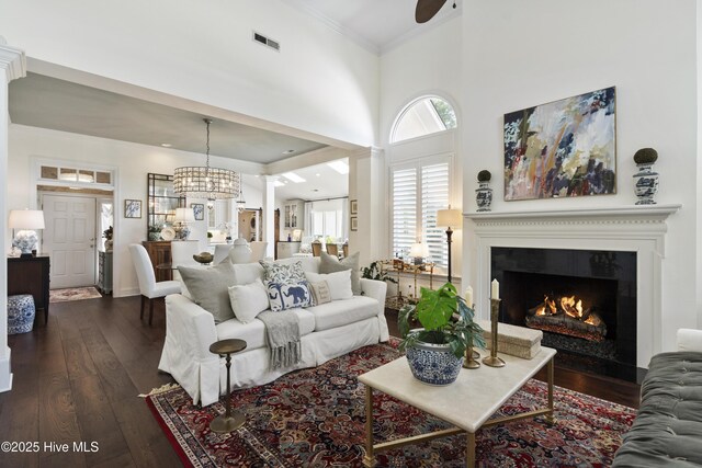 living area featuring dark wood-style flooring, healthy amount of natural light, a warm lit fireplace, ornamental molding, and a towering ceiling